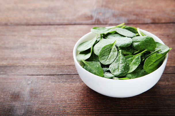 Spinach leaves in bowl on brown wooden table - Fotografie, Obrázek