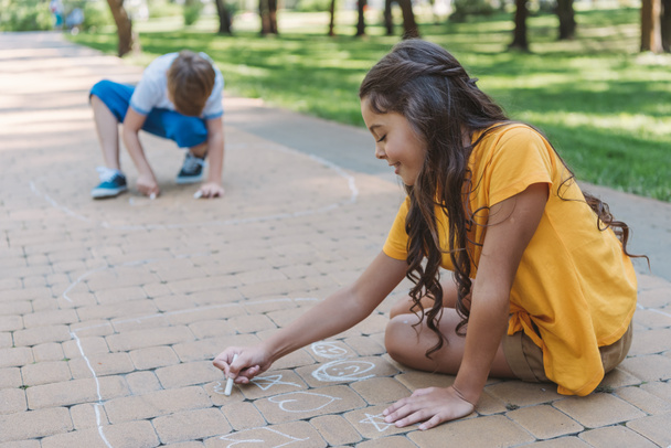 adorable smiling children drawing with chalk in park  - Zdjęcie, obraz