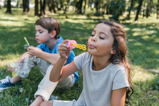 adorable kids sitting and blowing soap bubbles in park - Foto, Imagem