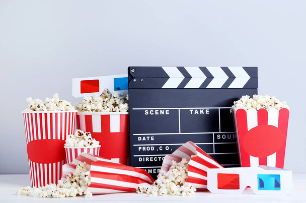 Clapper board with popcorn in striped buckets and glasses on grey background - Foto, Imagem