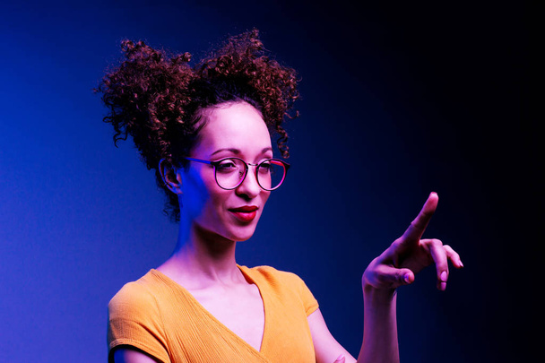 intelligentes Mädchen mit Brille und erhobenem Finger, das auf etwas drückt oder zeigt, isoliert auf dunkelblauem Hintergrund - Foto, Bild