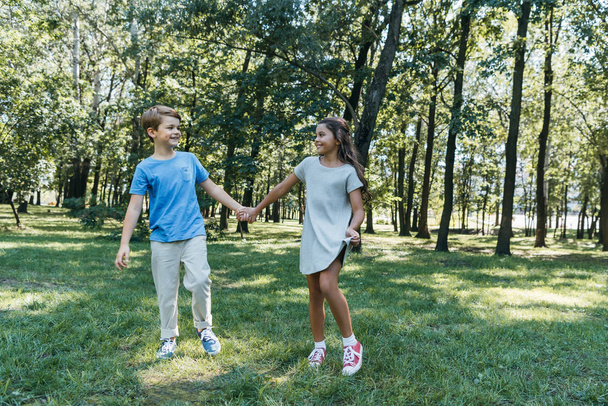 adorable happy kids holding hands and smiling each other in park - Photo, Image