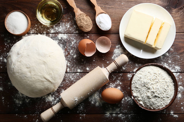 Raw dough with butter, eggs and rolling pin on wooden table - Valokuva, kuva