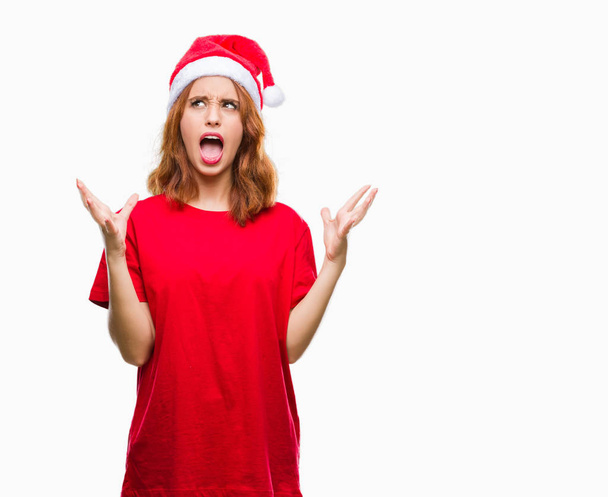 Young beautiful woman over isolated background wearing christmas hat crazy and mad shouting and yelling with aggressive expression and arms raised. Frustration concept. - Фото, изображение