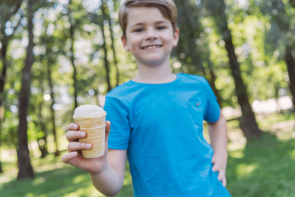 close-up view of happy child holding ice cream and smiling at camera in park - Foto, Imagem