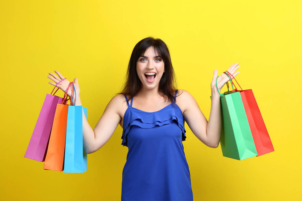 Young woman with shopping bags on yellow background - Foto, immagini