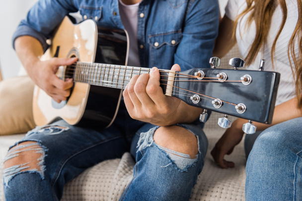 partial view of man playing on acoustic guitar while his girlfriend sitting near on couch at home - Fotoğraf, Görsel