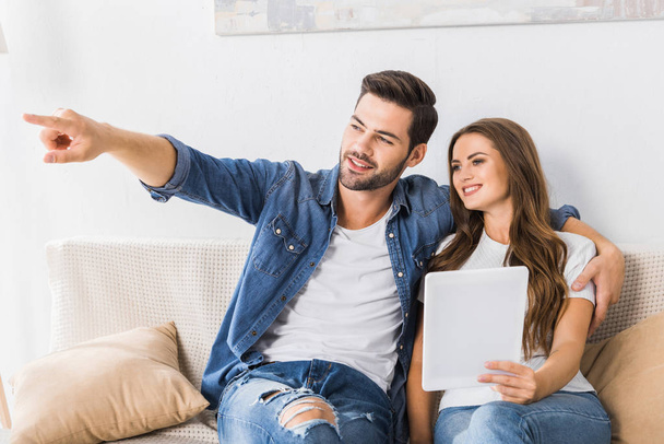 handsome young man pointing by finger to girlfriend with digital tablet on couch at home  - Foto, immagini