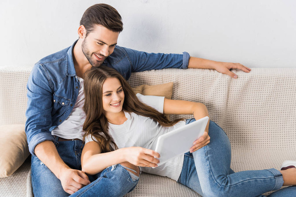 happy young couple watching digital tablet on couch at home - Fotó, kép