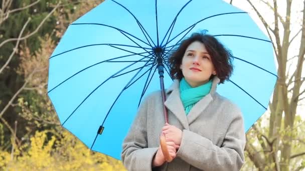 Hezká mladá žena červené hlavy s modrý deštník na mostě na jaře parku. Zelené stromy a pozadí květy Zlatice. - Záběry, video