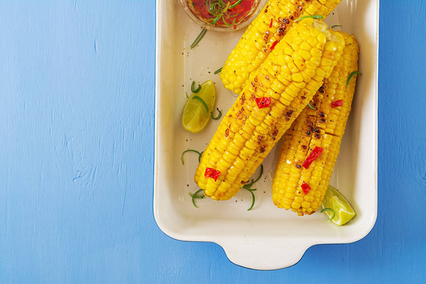 Grilled sweet corn with mexican sauce, chilli and lime on blue background. Healthy summer food. Top view. Flat lay - Photo, image