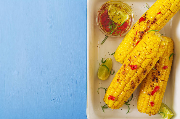 Grilled sweet corn with mexican sauce, chilli and lime on blue background. Healthy summer food. Top view. Flat lay - Photo, image