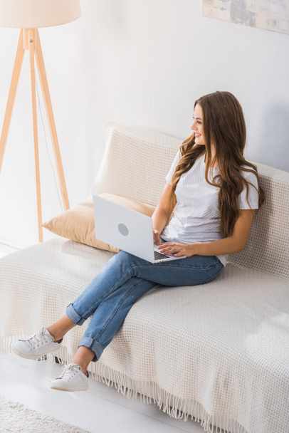 自宅のソファでノート パソコンを操作笑みを浮かべて女性フリーランサーのハイアングル  - 写真・画像