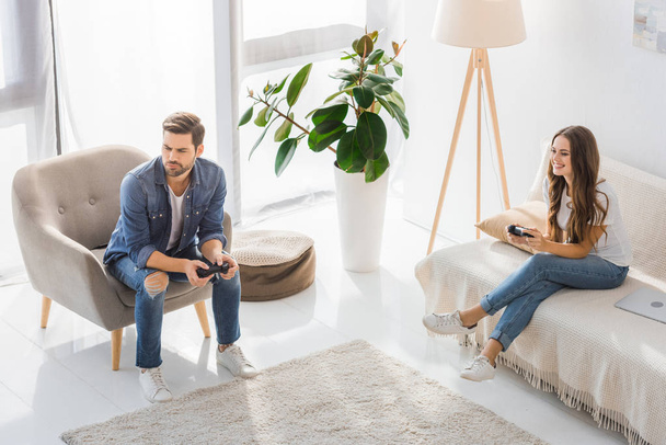 high angle view of upset young man playing video game with smiling girlfriend at home  - Photo, Image