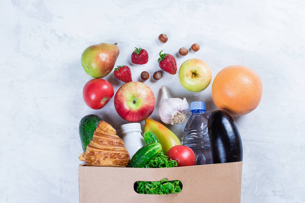 Täysi ruokapaperi laukku terveellistä ruokaa hedelmiä ja vihanneksia valkoisella pöydällä taustalla. Huippunäkymä. Litteä pano. Kopioi tila
 - Valokuva, kuva