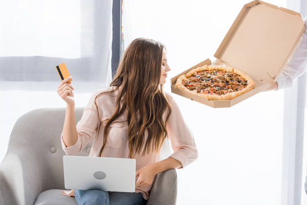 partial view of man with pizza in paper box and young woman with credit card and laptop at home, shopping online concept - Fotó, kép