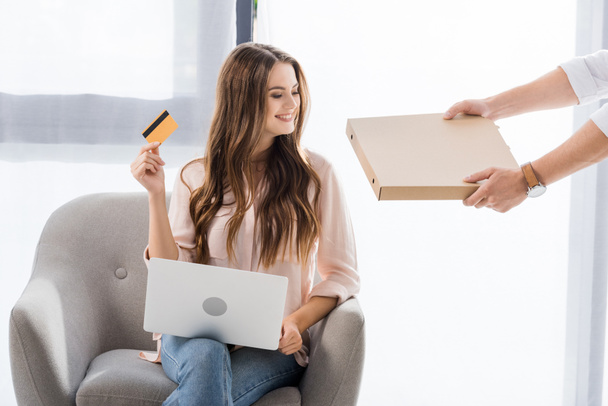 partial view of man with pizza in paper box and smiling woman with credit card and laptop at home, shopping online concept - Φωτογραφία, εικόνα