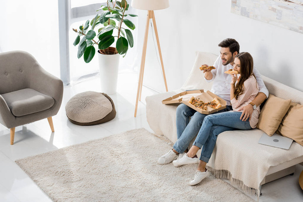 korkea kulma näkymä nuori pari syö pizzaa katsellessaan televisiota kotona
 - Valokuva, kuva