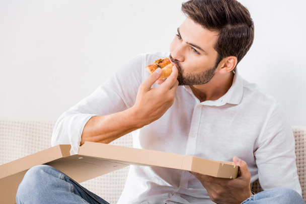 portrait of young man eating pizza alone at home - Foto, Bild