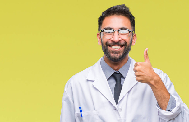 Adult hispanic scientist or doctor man wearing white coat over isolated background doing happy thumbs up gesture with hand. Approving expression looking at the camera with showing success. - Foto, imagen