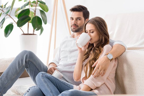 young loving couple with cups of coffee on sofa at home - Foto, Bild