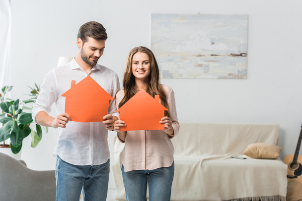 portrait of smiling couple showing paper houses in hands at new home - Photo, Image