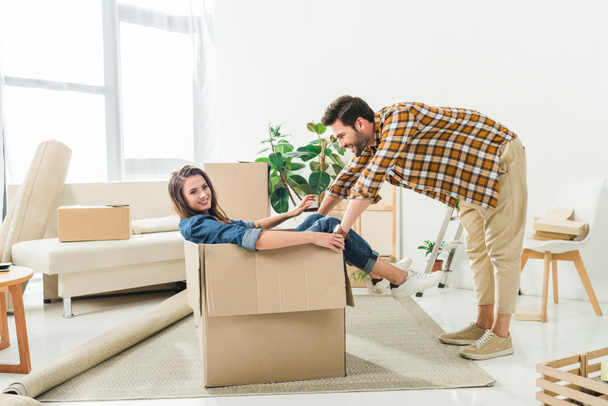 side view of couple having fun with cardboard box at new house, moving home concept - Photo, Image