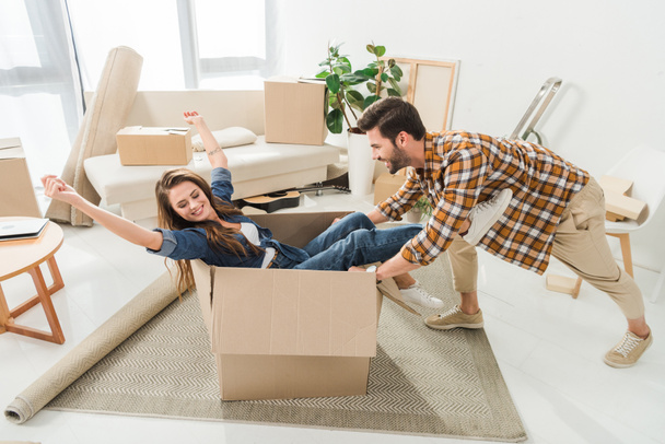 side view of couple having fun with cardboard box at new house, moving home concept - Foto, imagen