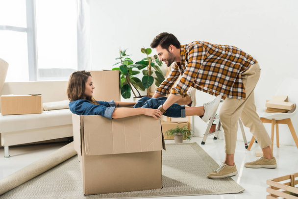 side view of couple having fun with cardboard box at new house, moving home concept - Fotó, kép
