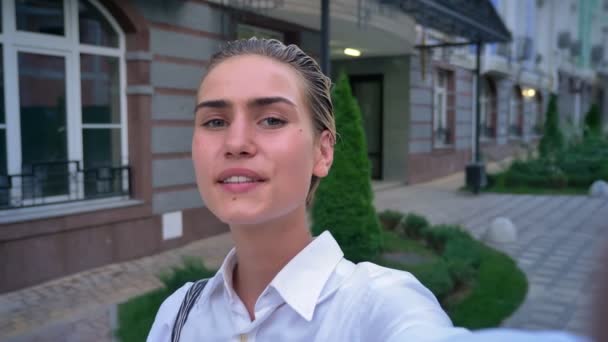Young modern woman is standing on street, holding camera, making selfie, communication concept - Video, Çekim