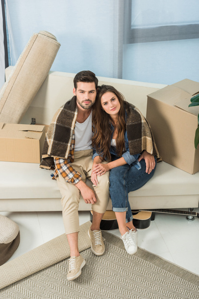 Blick auf verliebte Paare, die mit einer Decke bedeckt auf dem Sofa im neuen Haus ruhen - Foto, Bild