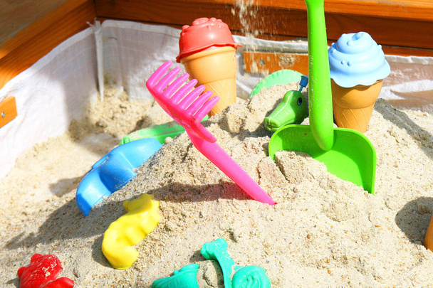 Падение песка в песочницу. Различные игрушки разного цвета. Красочная деревянная песочница для детей
. - Фото, изображение