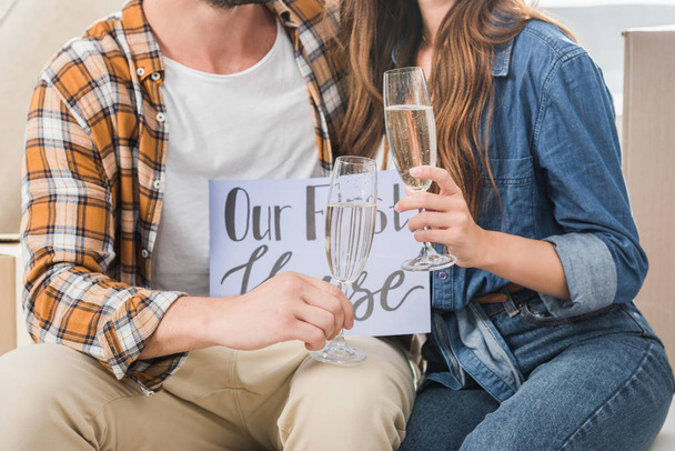 partial view of couple with glasses of champagne and our first house card, moving home concept - Photo, Image