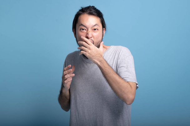 Young bearded man excited shocking pose in blue background. Very excited Asian young hipster with hand over mouth, surprise expression, half body shot. Young generation hipster concept. - Фото, зображення