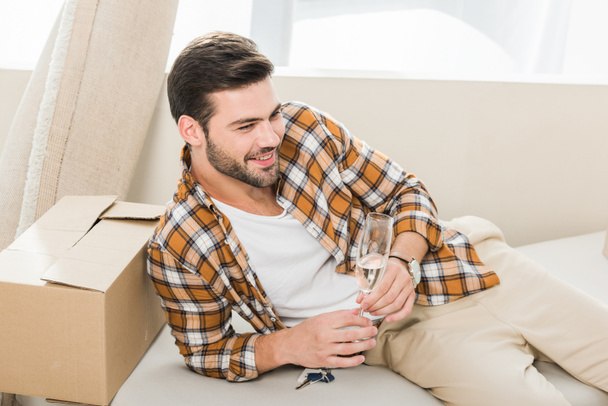 hymyilevä mies lasi samppanjaa lepää sohvalla uudessa kodissa, muuttamassa kotiin käsite
 - Valokuva, kuva