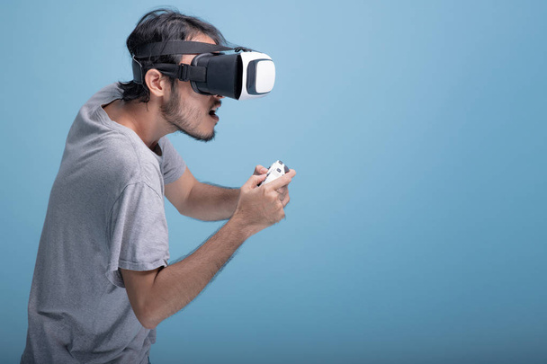 Young bearded man playing VR game in blue background. Extremely focus Asian young hipster wearing VR headset, half body shot. Young generation hipster relaxation concept. - Фото, зображення