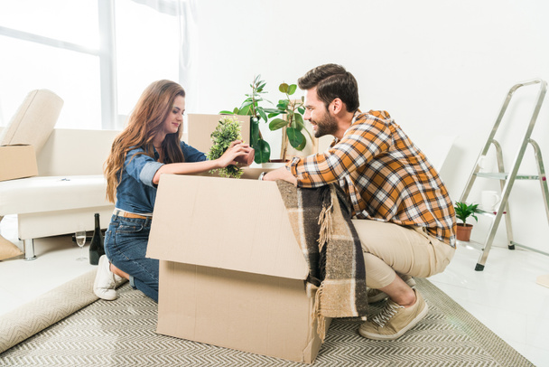 side view of young couple unpacking cardboard boxes together at new home, moving home concept - Foto, imagen
