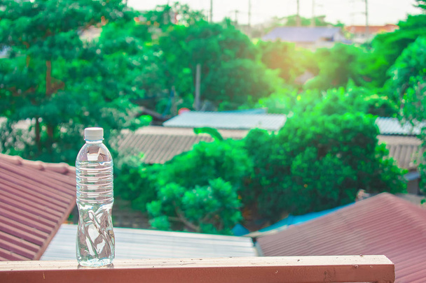Láhev vody z plastu na obloze s domácí a strom bokeh rozmazané - Fotografie, Obrázek