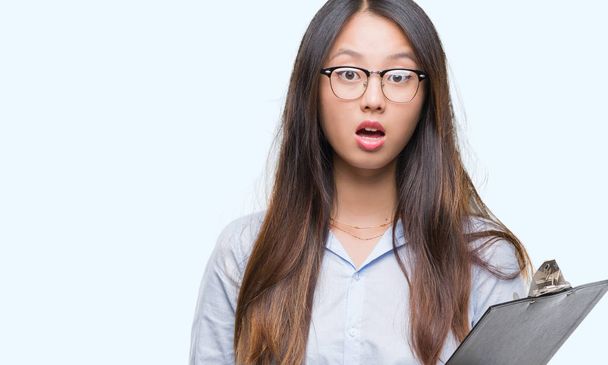 Молодая азиатская бизнес-женщина держит планшет на изолированном фоне напуганный в шоке с неожиданным лицом, напуганный и взволнованный выражением страха
 - Фото, изображение