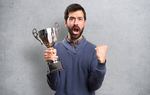 Щасливий красивий брюнетка людина з бородою тримає трофей на текстурованому фоні
 - Фото, зображення