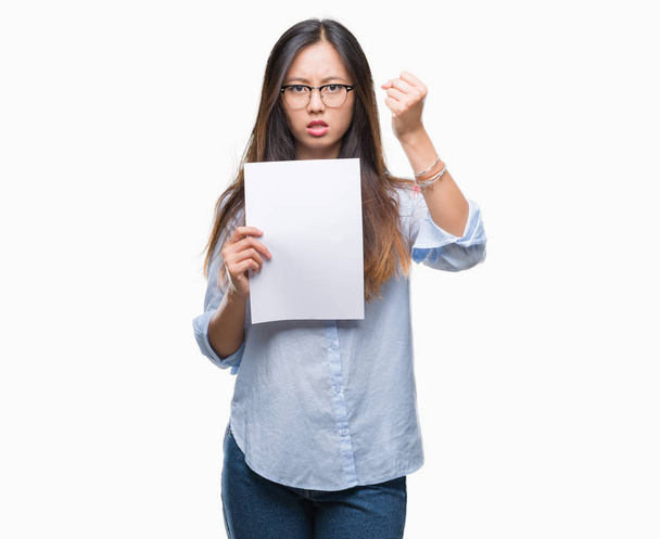 Jonge Aziatische vrouw bedrijf blanco papier over geïsoleerd background boos en gefrustreerd schreeuwen met woede, gek en schreeuwen met opgeheven hand, woede concept - Foto, afbeelding