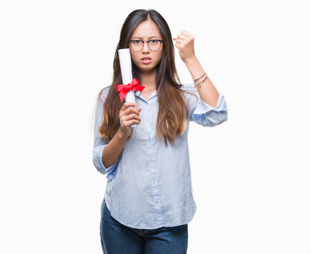 Young asian woman holding degree over isolated background annoyed and frustrated shouting with anger, crazy and yelling with raised hand, anger concept - Photo, Image