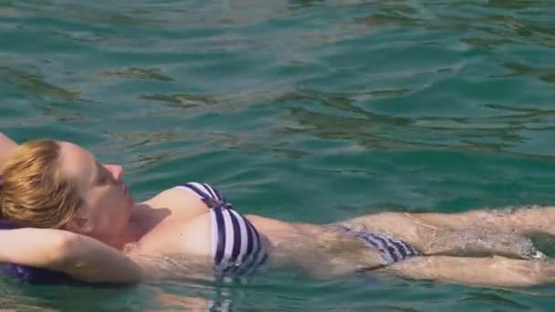 Eine Frau ohne Make-up ruht sich aus. Ein Mädchen schwimmt auf dem Rücken auf einem aufblasbaren Kissen im Meer. 4k Zeitlupe - Filmmaterial, Video