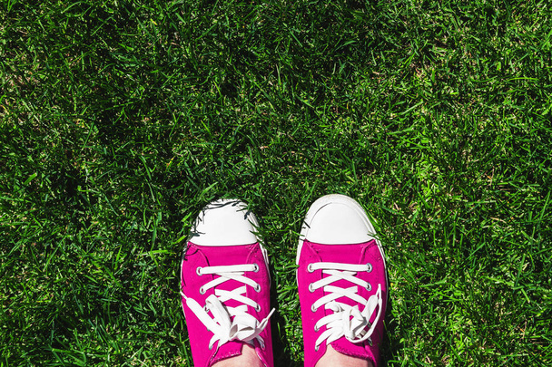 Ноги в старых розовых кроссовках на зеленой траве. Вид сверху. Концепция молодости, весны и свободы
. - Фото, изображение