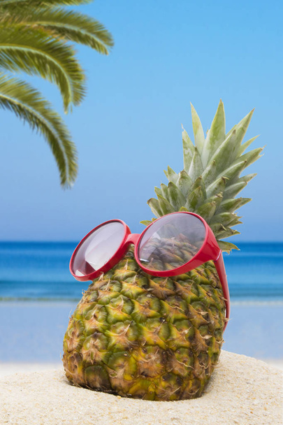 pineapple with sunglasses in the summer landscape on the beach - Photo, Image