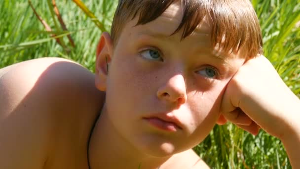 Portrait of cute red-haired teenager after swimming in a river in summer against a background of green grass. Boy teenager with freckles and blue eyes looking at sides - Footage, Video