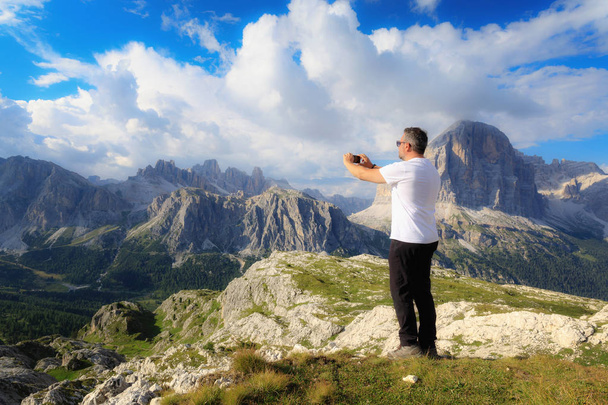 Immersed in the beautiful alpine scenery, a man takes a picture with his cell phone to the high-altitude landscape with the mountain peaks and the cloudy sky. - Photo, Image