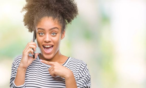 Joven mujer afroamericana hablando por teléfono sobre fondo aislado muy feliz señalando con la mano y el dedo
 - Foto, imagen