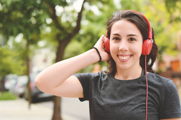 Portrait of young beautiful woman with red headphones listening music. Outdoors. Urban concept. - Foto, immagini