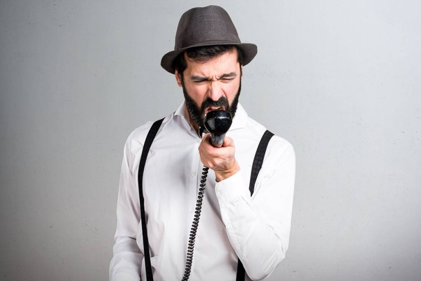 Hipster άνδρας με γενειάδα που μιλάμε για vintage τηλέφωνο σε γκρίζο φόντο - Φωτογραφία, εικόνα
